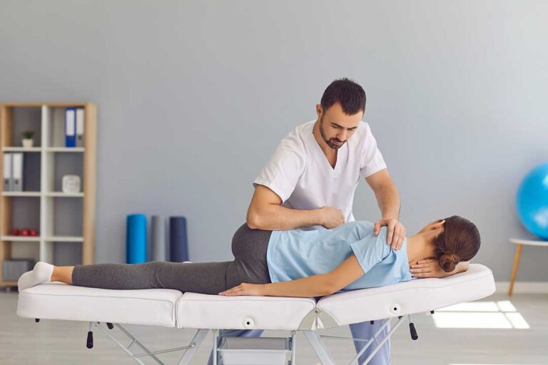 A chiropractor gently adjusting an athlete's knee on a padded treatment table.