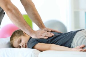 A chiropractor performing a gentle back adjustment on an adult patient in a calm, clinical setting.